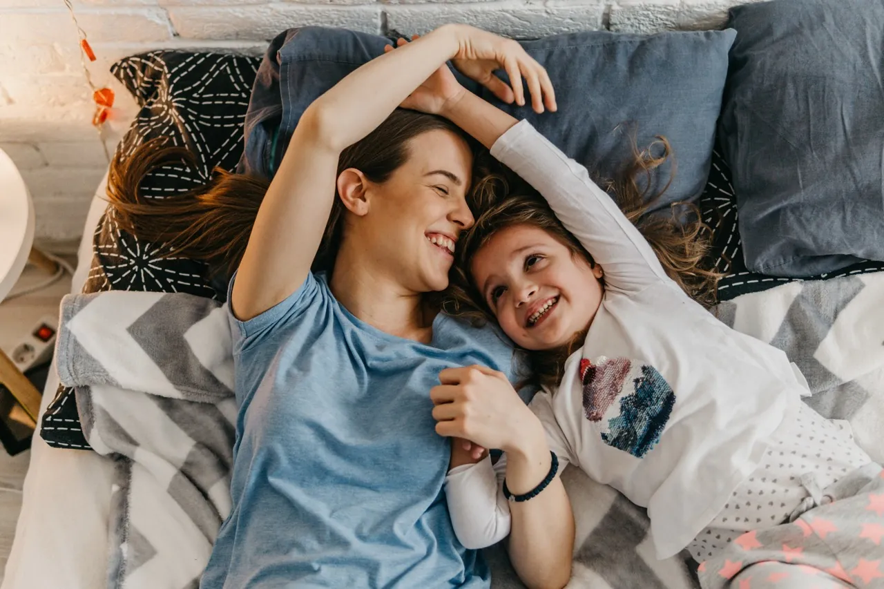 Babysitterin und Mädchen liegen lachend auf dem Sofa