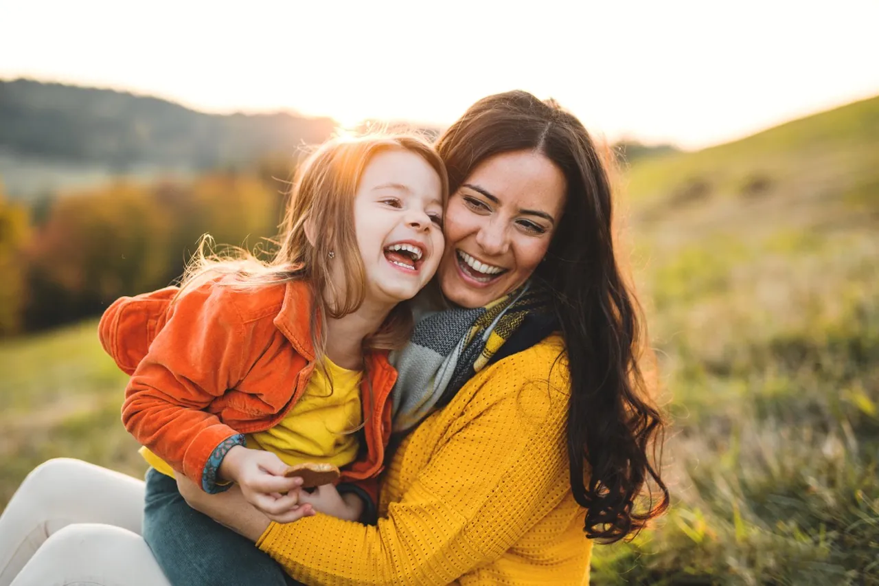 Mutter und Tochter lachen eng umarmt auf einer herbstlichen Wiese