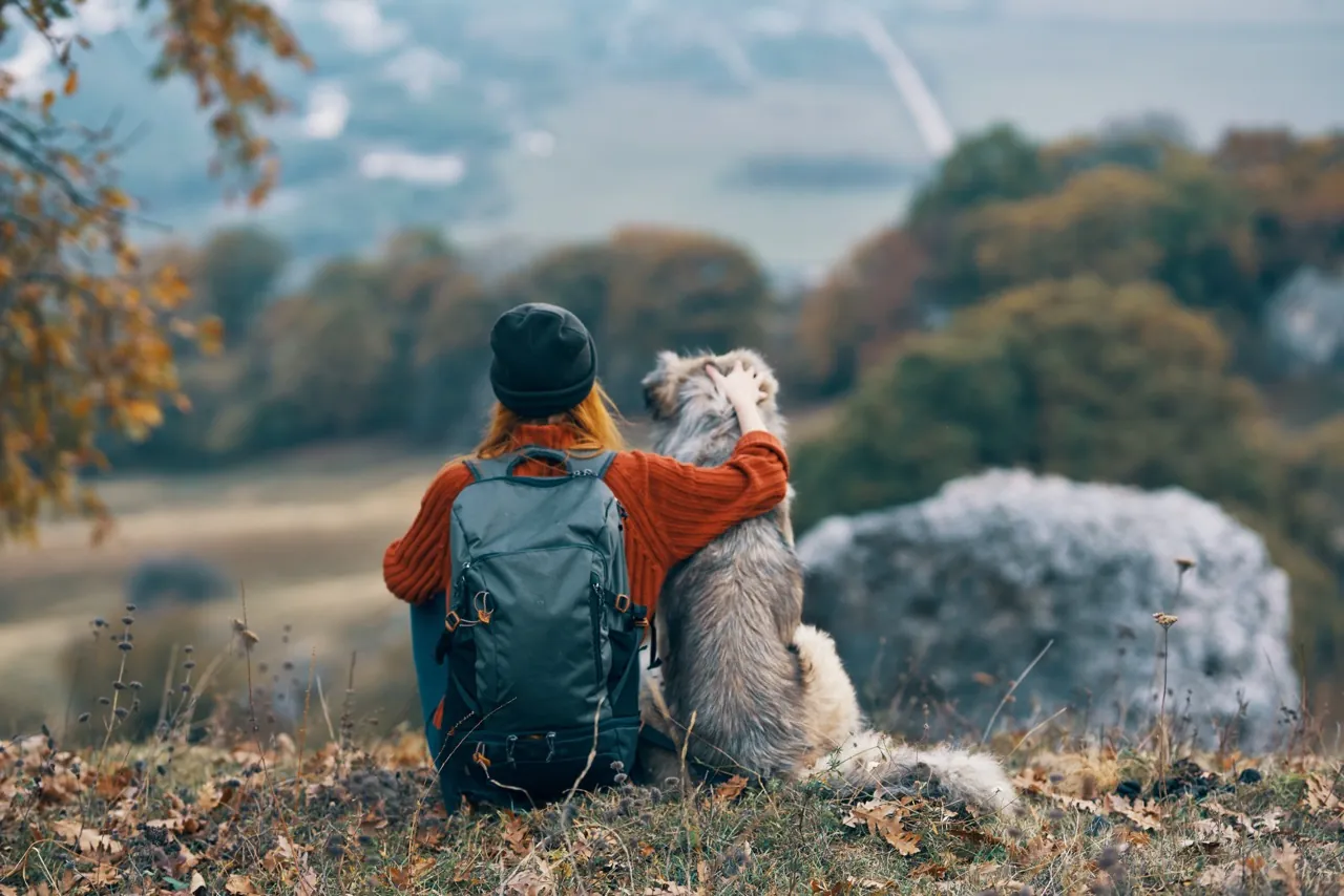 Frau sitzt mit einem Hund auf einem Felsen und schaut in die Landschaft
