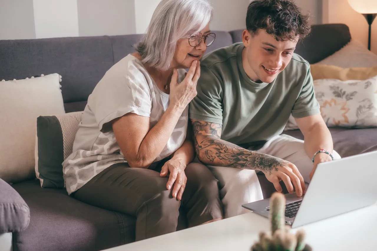 Seniorin und junger Mann schauen gemeinsam auf den Laptop