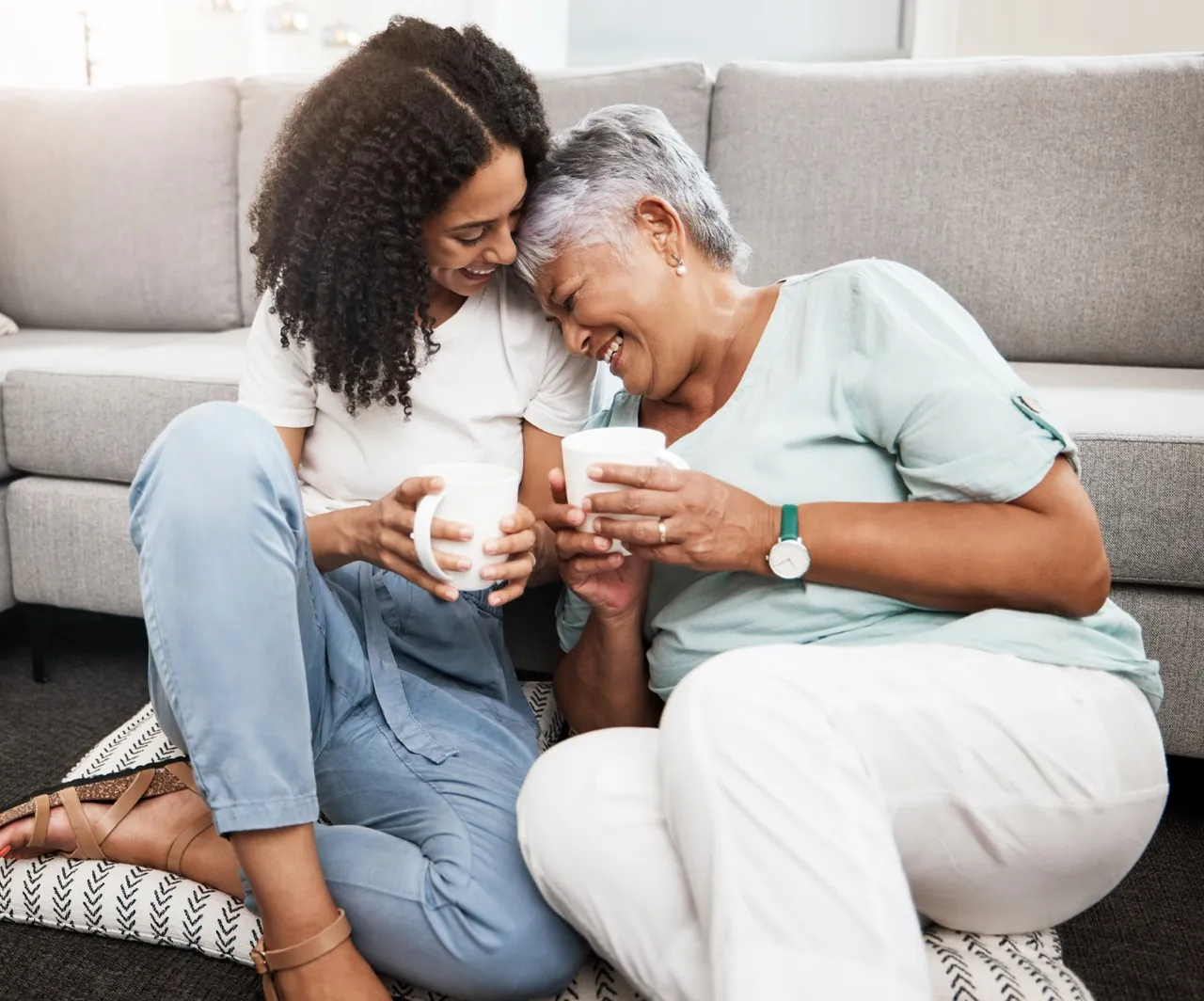 Seniorin und junge Frau lachen gemeinsam auf dem Sofa
