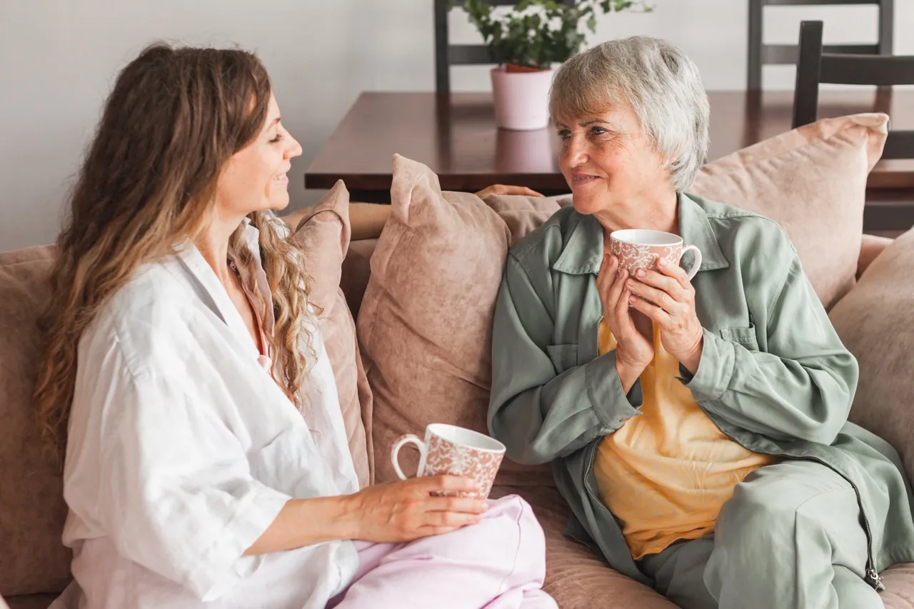 Alltagshilfe und Seniorin trinken gemeinsam Tee auf dem Sofa