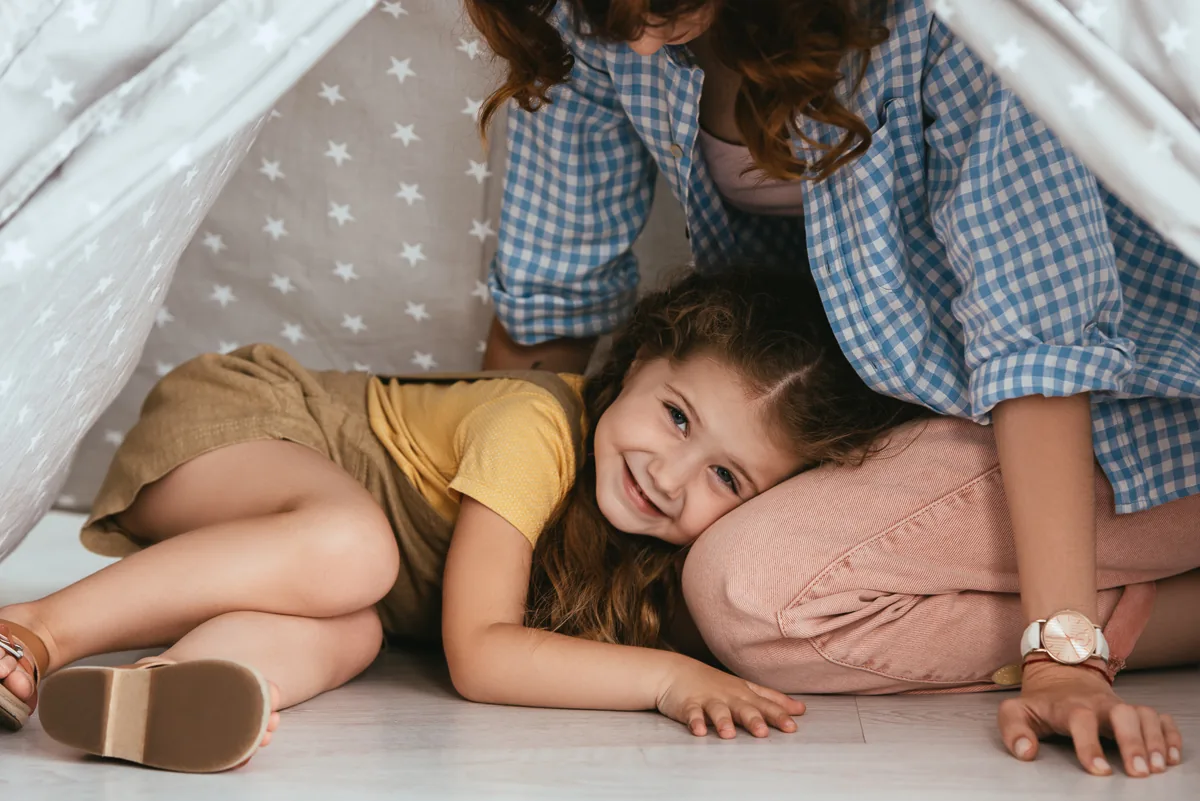 Ausschnitt eines Babysitters und eines glücklichen Kindes, das vom Spielzelt aus in die Kamera schaut