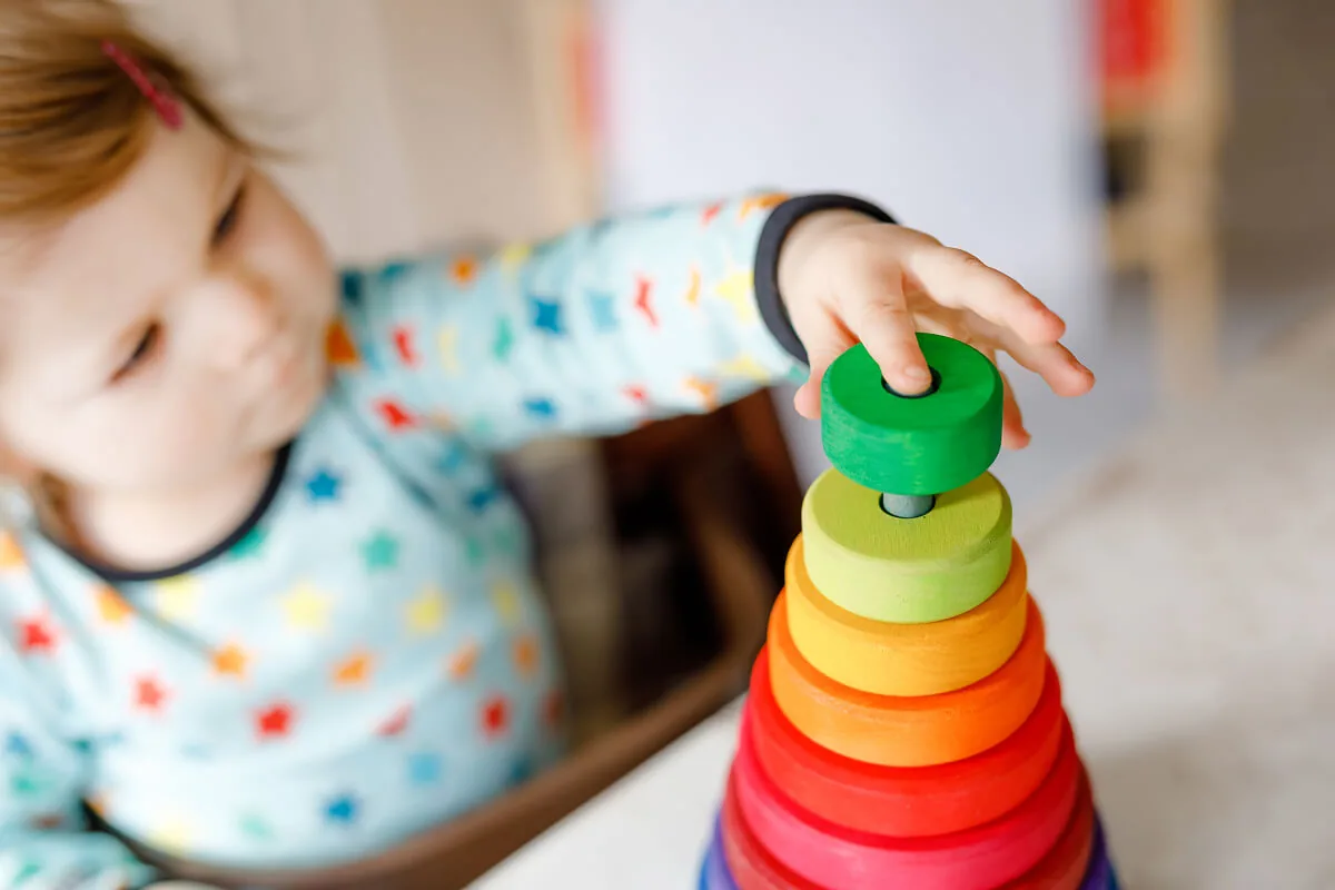 Ein Kleinkind spielt mit einem Turm aus Holzspielzeug