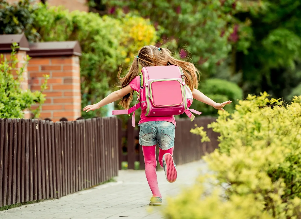 Kleines Mädchen mit Schulmappe ist auf dem Weg zur Schule