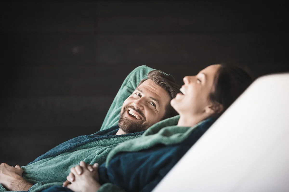 Ein Paar sitzt auf Liegestühlen in einem Wellness-Hotel. Sie entspannen sich.