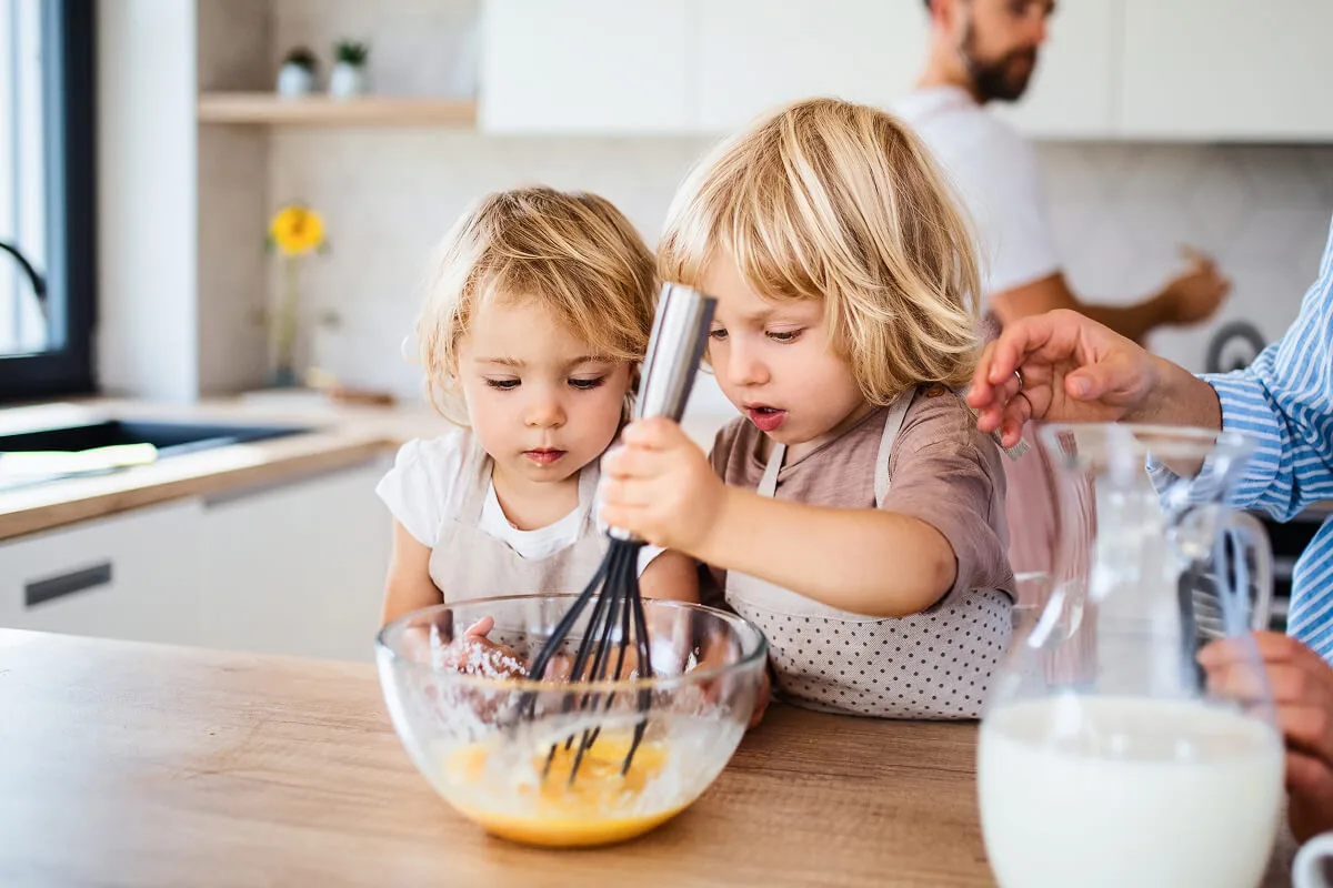 Zwei kleine Kinder sind der Küche und rühren in einer Schüssel mit Teig