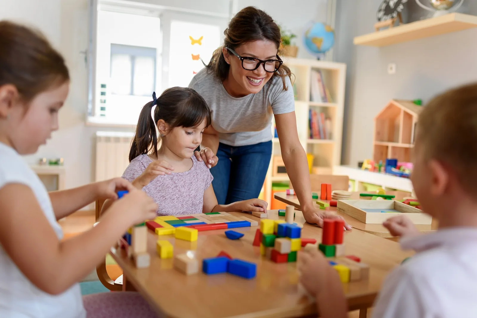 Eine Tagesmutter spielt mit 3 Kindern mit Holzbausteinen