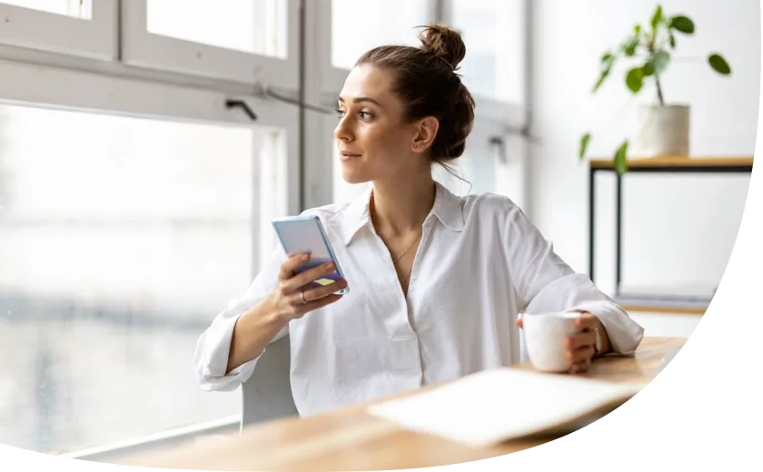 Eine Mutter sitzt mit einem Kaffee und ihrem Smartphone am Tisch und sucht online einen Babysitter