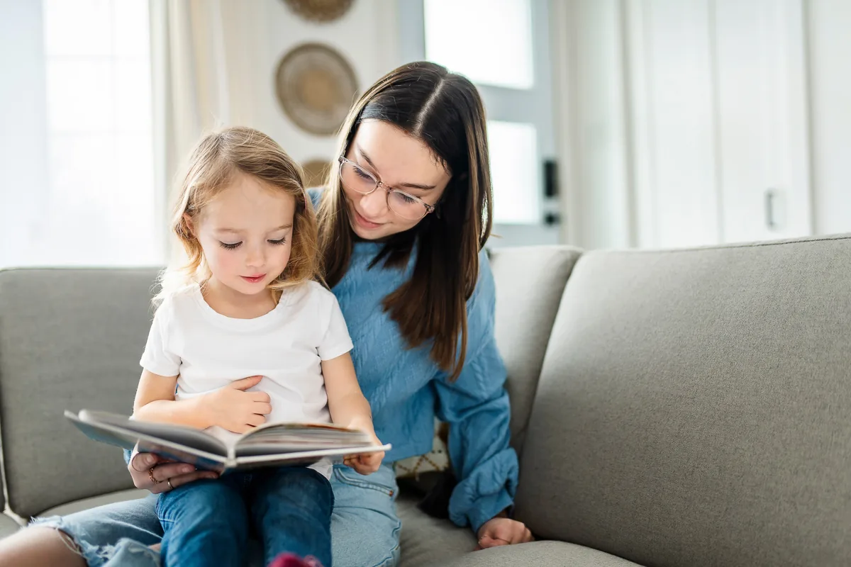 Ein glückliches Kind sitzt auf dem Sofa mit einer Nanny, die ein Buch hält