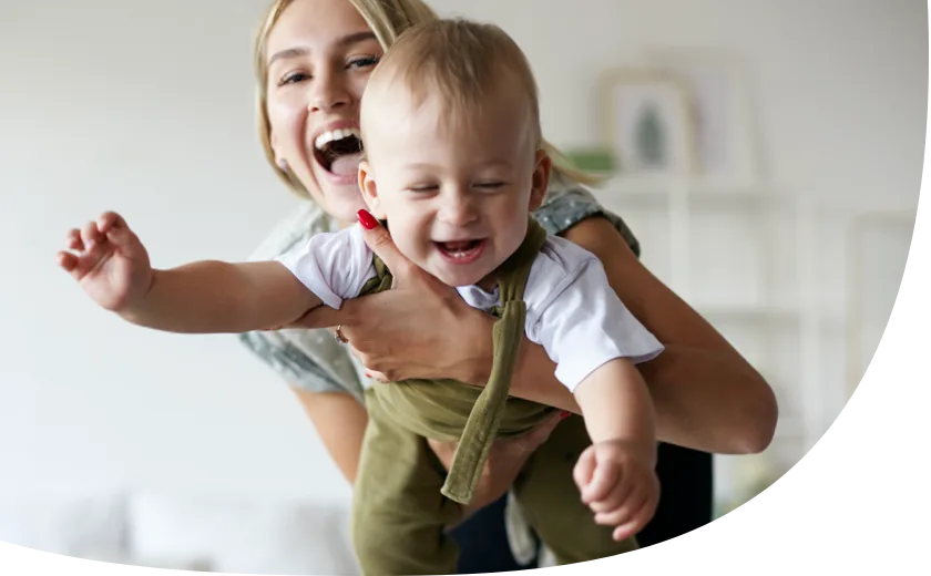 Nanny hält Baby im Arm. Die beiden lachen gemeinsam und haben Spaß